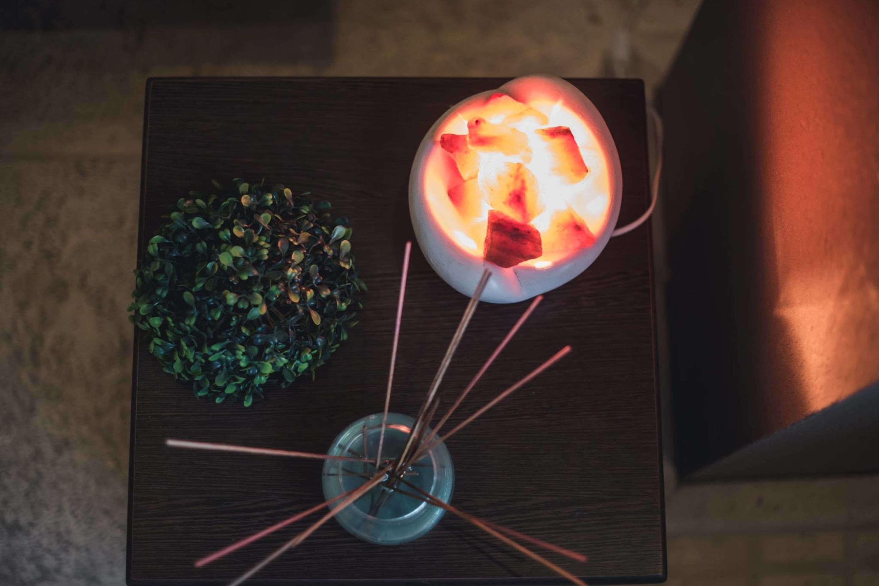Una mesa con una lámpara brillante, una planta pequeña en maceta y un vaso con una vela.
