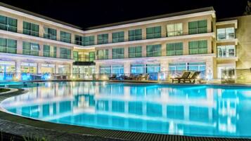 A hotel with a large outdoor swimming pool, multiple balconies, and a well-lit facade.