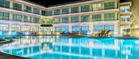 Un hotel con una amplia piscina al aire libre, varios balcones y una fachada bien iluminada.