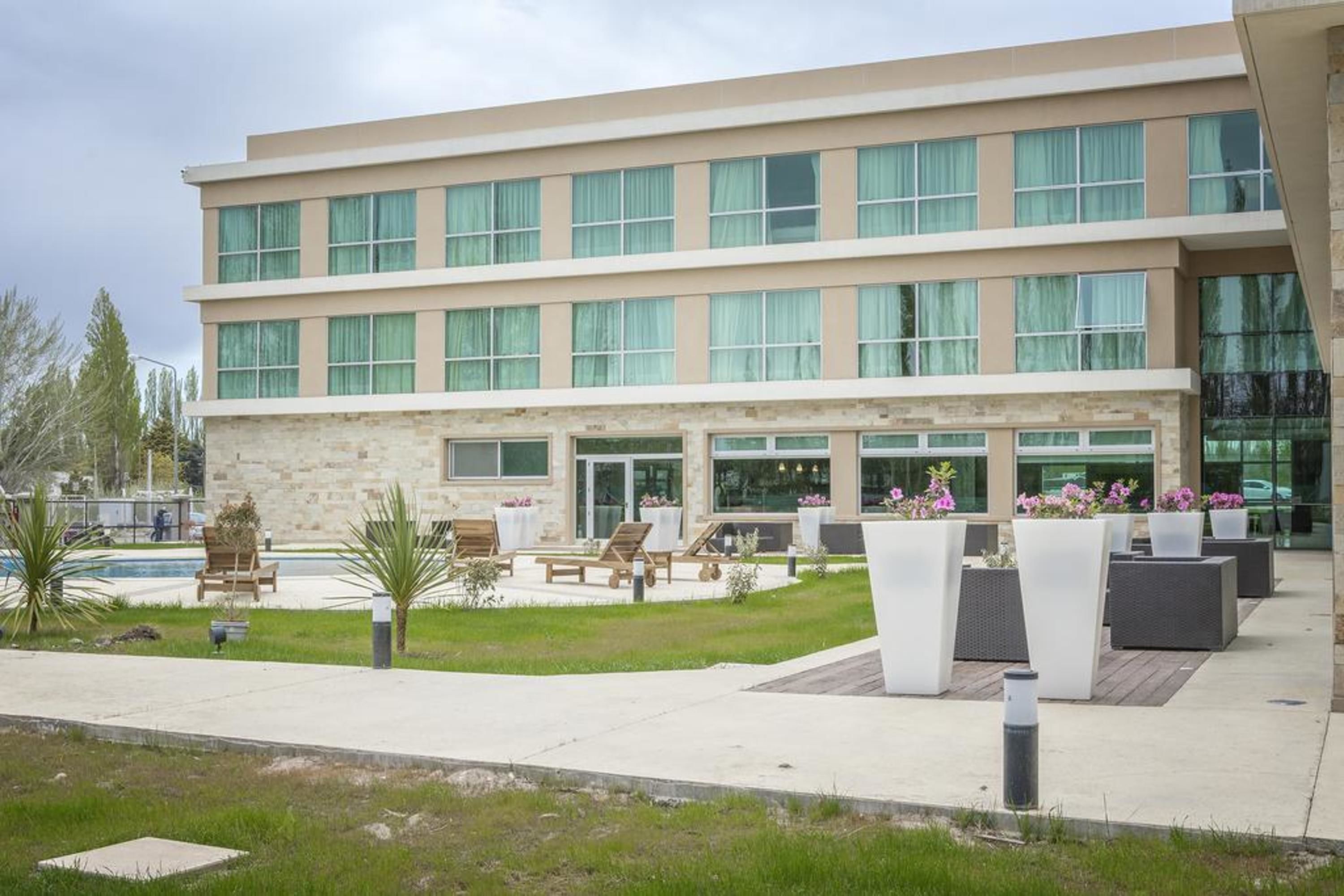 A modern hotel with a stone facade, multiple balconies, outdoor seating, and a pool area.