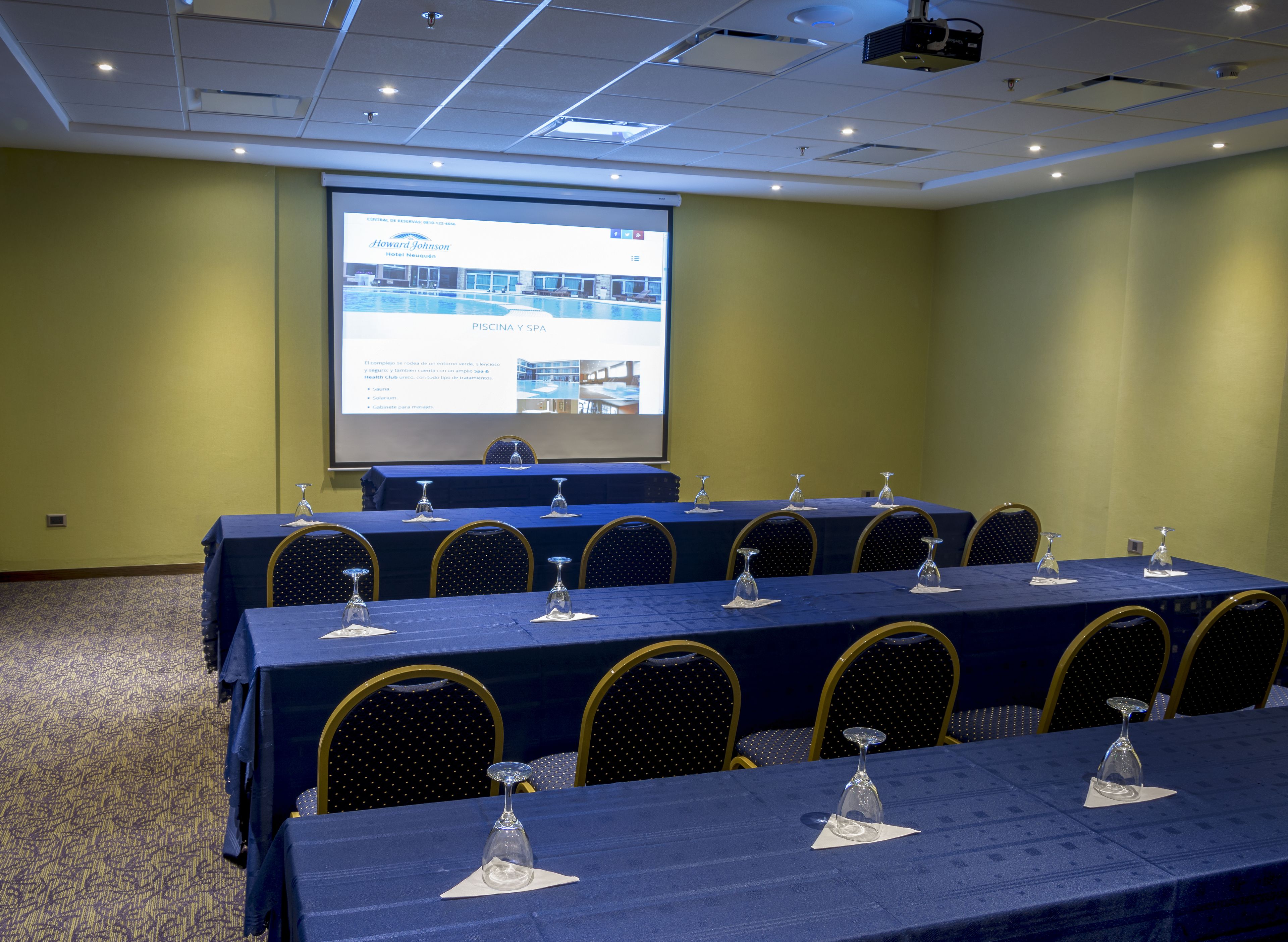 Un salón de conferencias con una larga mesa dispuesta para una reunión, equipado con sillas y copas de vino.