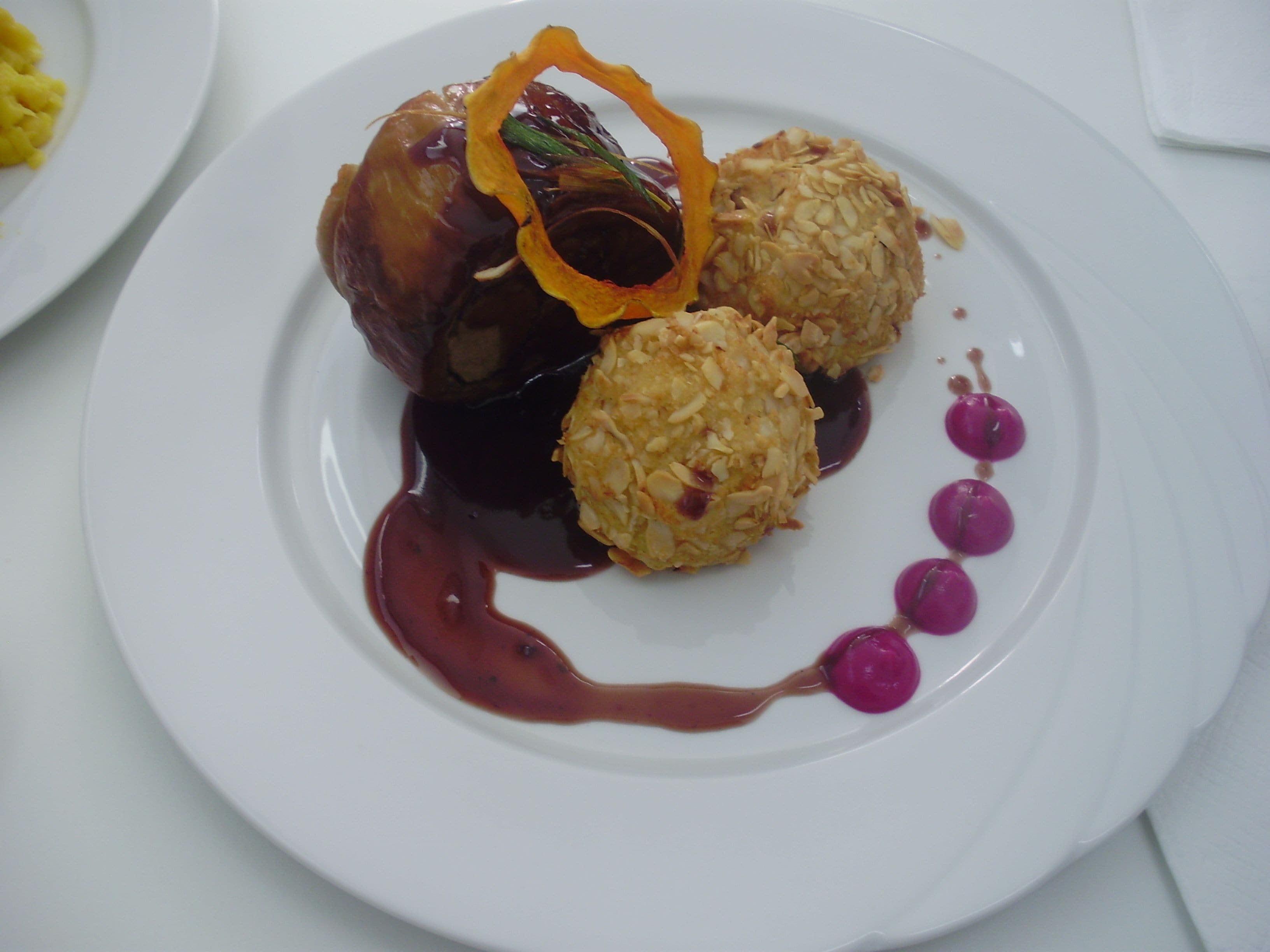 Un plato con un postre que incluye fruta caramelizada, dos bolas de arroz redondas y una salsa decorativa.