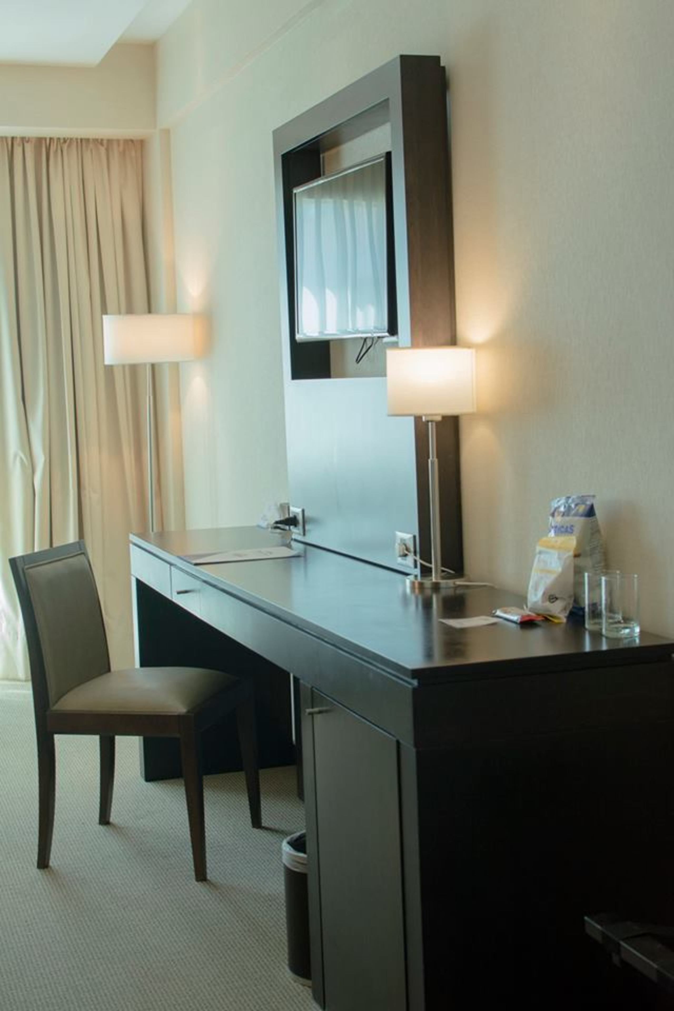 A hotel room with a desk, chair, and a small trash bin.