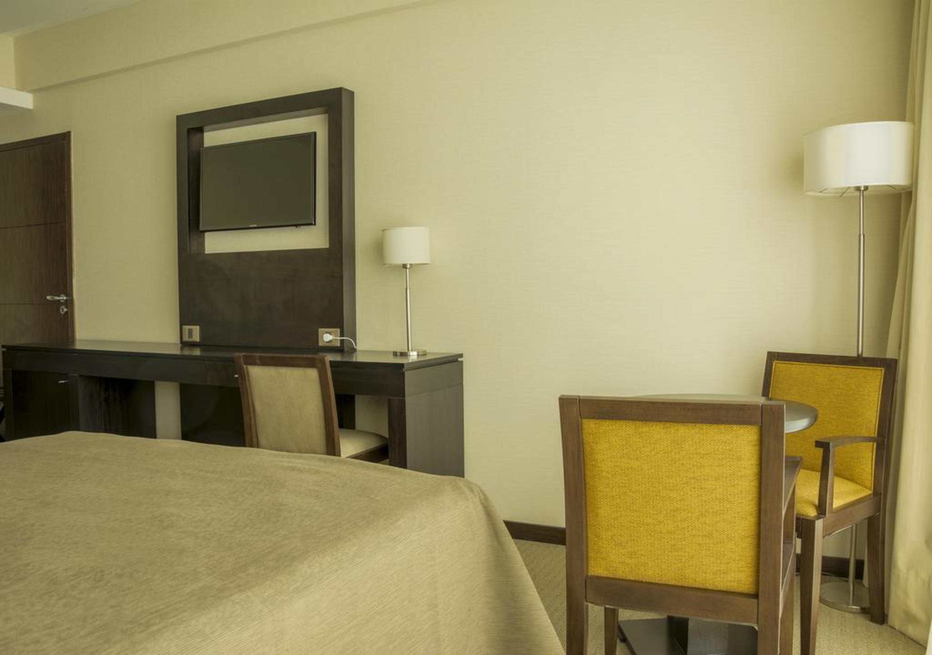 Una habitación de hotel con cama, escritorio, silla, lámpara y televisión.