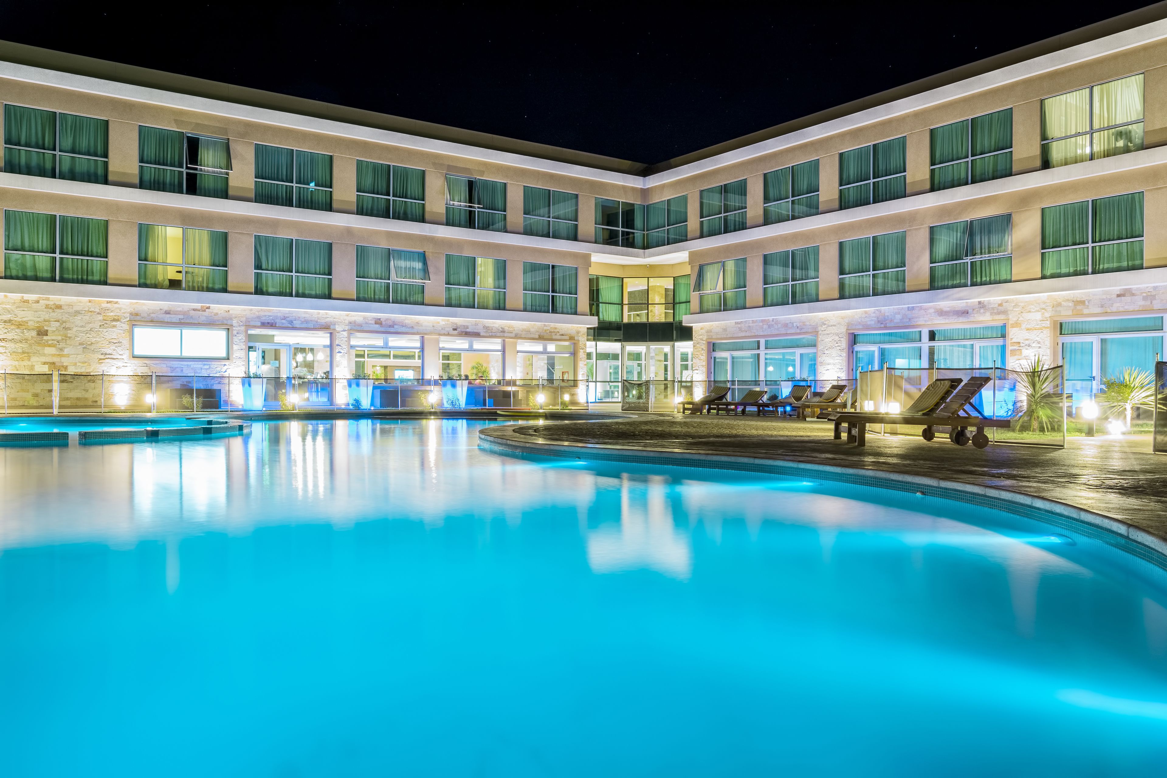 Un hotel con una amplia piscina exterior, varios balcones y una fachada bien iluminada.