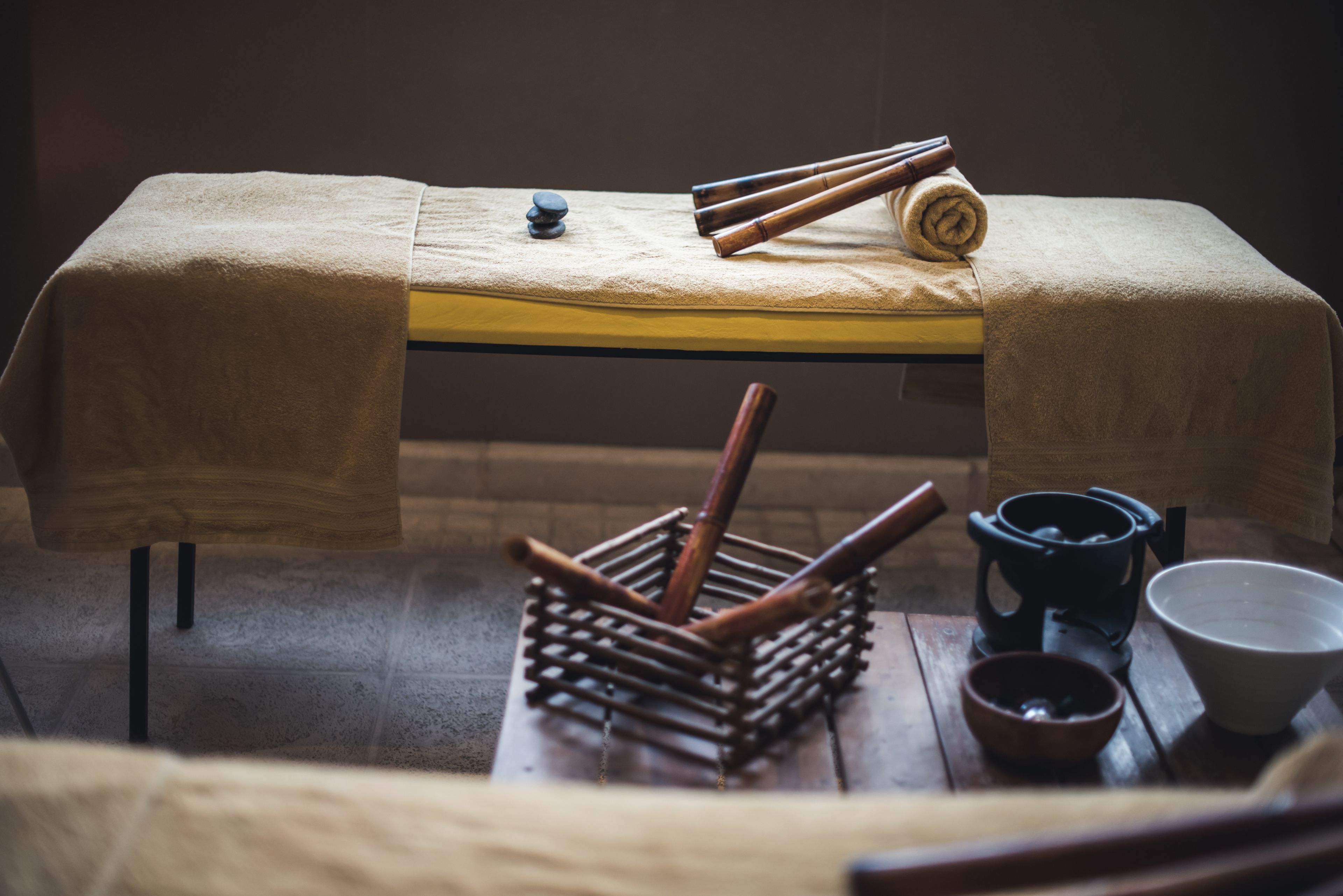 A massage table with towels, a wooden massage tool set, a black kettle, and a bowl.