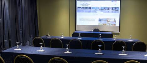 A conference room with a long table, chairs, and a projector screen displaying hotel information.
