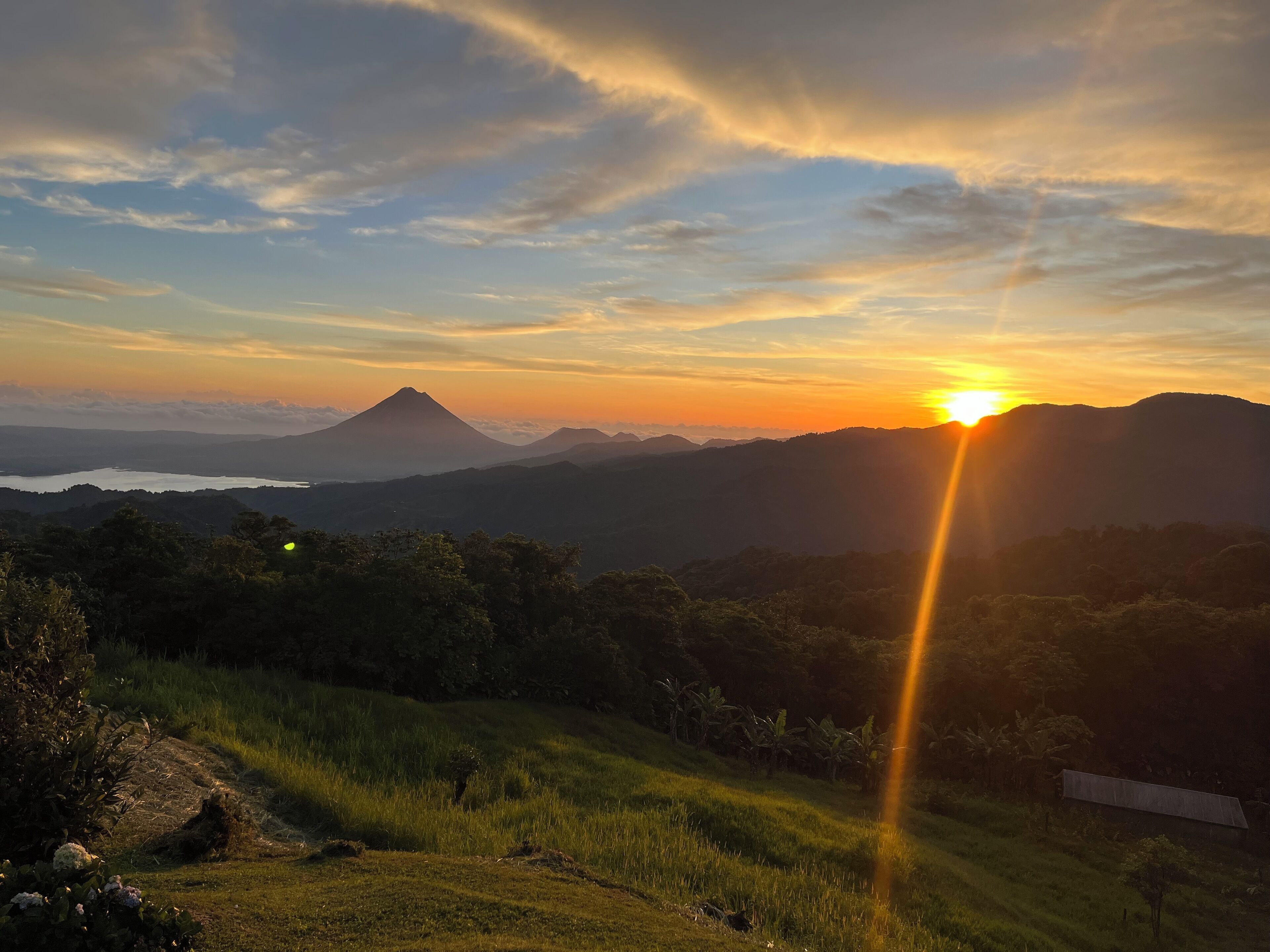Un paisaje con montaña, un cuerpo de agua y un atardecer.