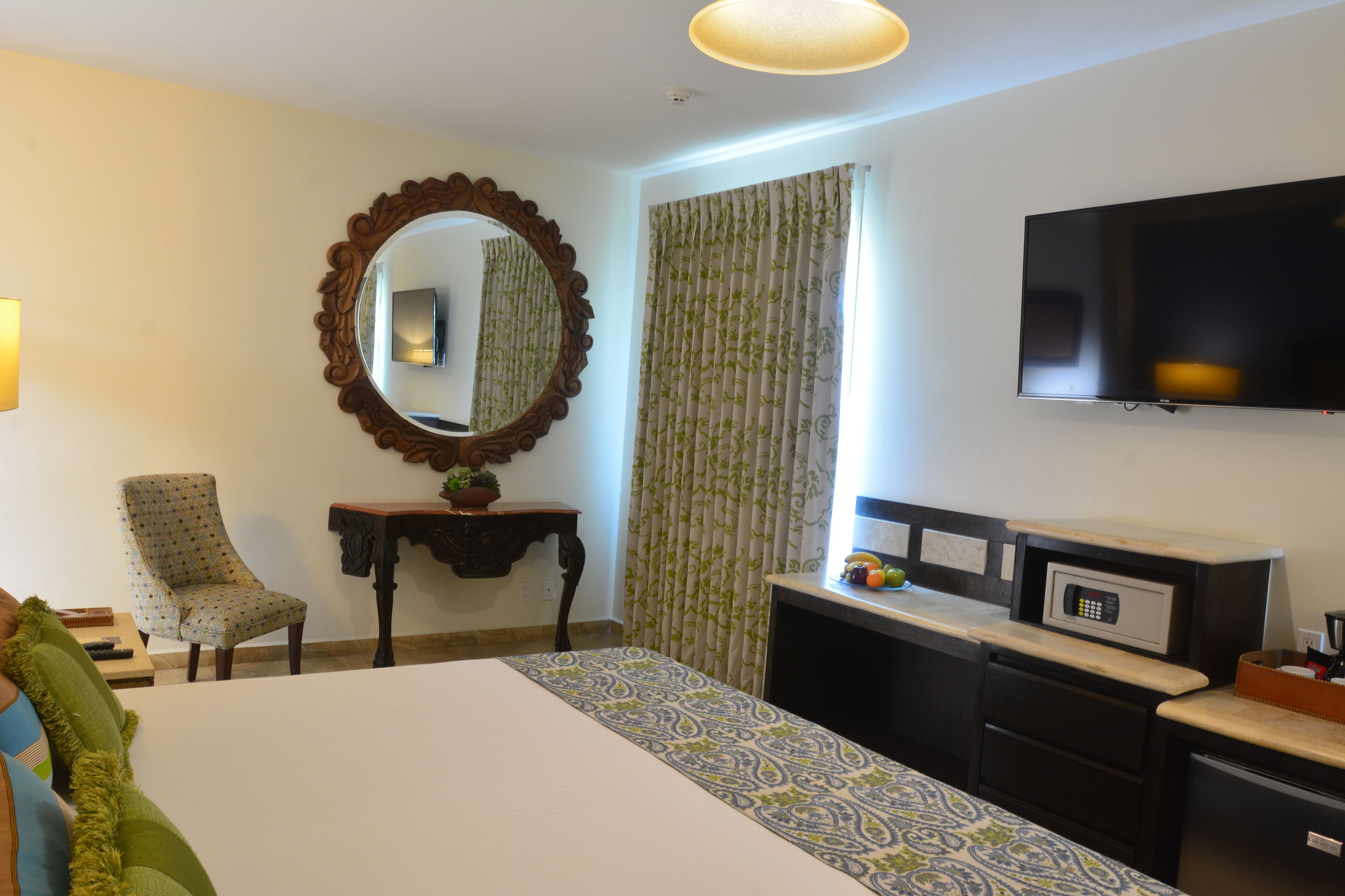 Quarto de hotel com cama, escrivaninha, televisão e espelho.