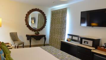 Quarto de hotel com cama, escrivaninha, televisão e espelho.