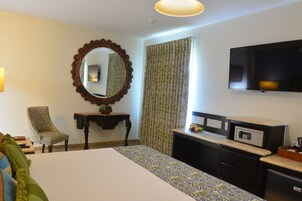 Quarto de hotel com cama, escrivaninha, televisão e espelho.