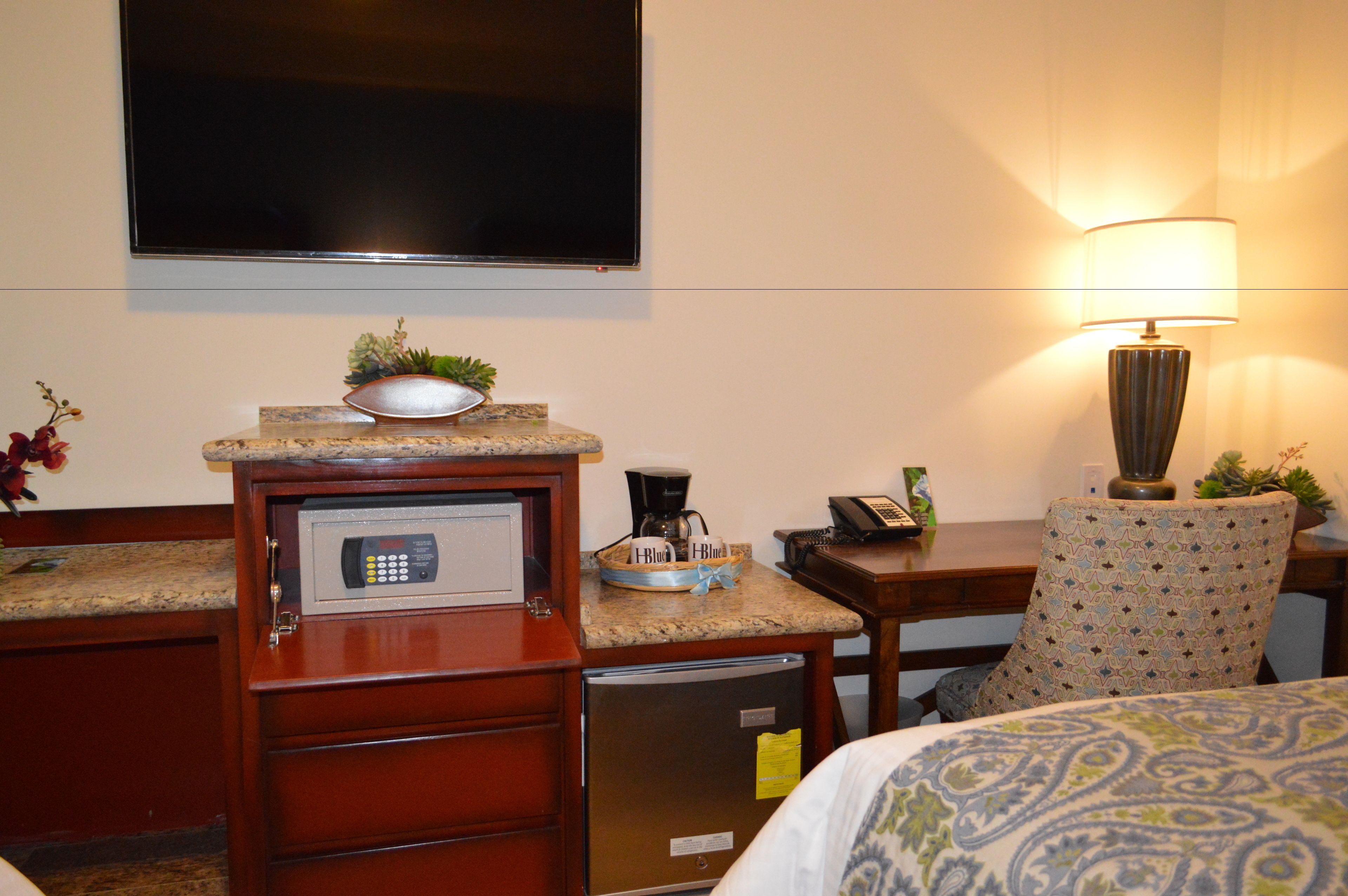 A hotel room with a bed, a desk with a coffee maker, a microwave, a refrigerator, a TV, and a lamp.
