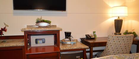 A hotel room with a bed, a desk with a coffee maker, a microwave, a refrigerator, a TV, and a lamp.