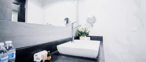 Um banheiro moderno com pia branca, duas espelhas, bancada preta e um vaso de planta.