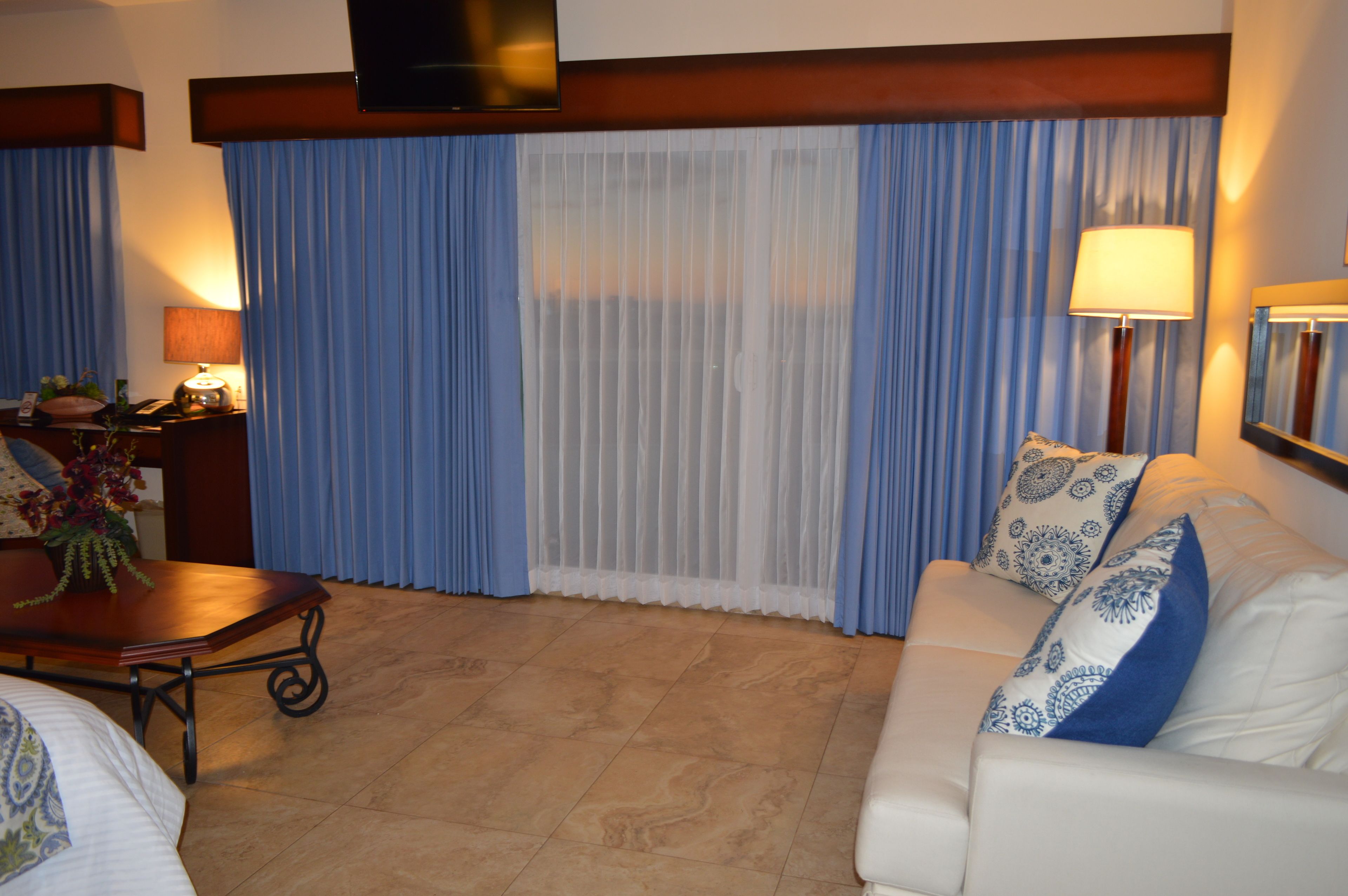 Una sala de estar con un sofá, una mesa de centro, una lámpara y un televisor montado en la pared.