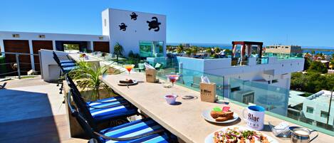 Una terraza en la azotea con piscina, sillas de descanso y vistas al océano.