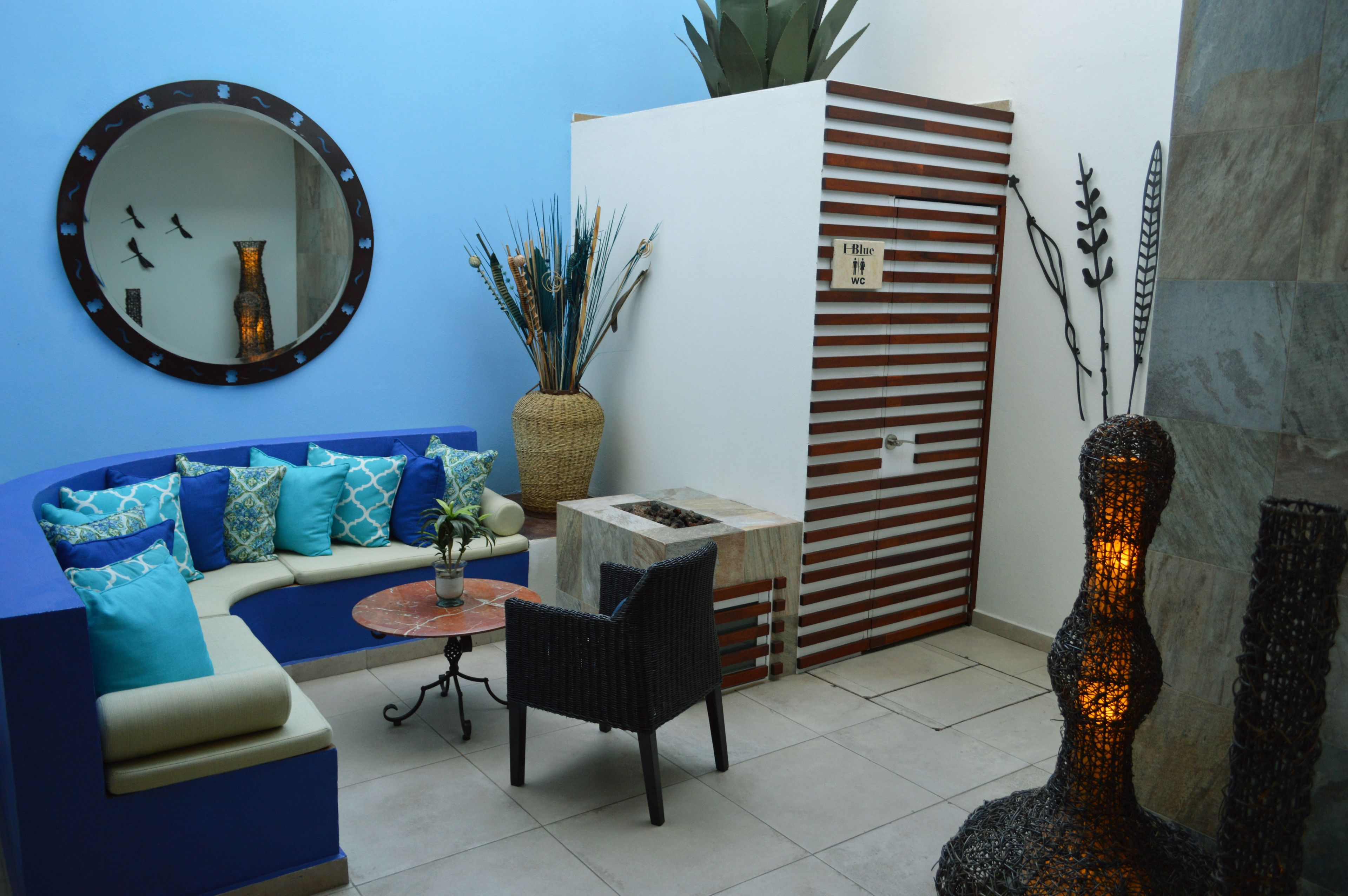 Una sala de estar moderna con un sofá azul, un espejo redondo, una mesita pequeña y un jarrón decorativo.