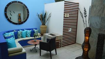 Una sala de estar moderna con un sofá azul, un espejo redondo, una mesita pequeña y un jarrón decorativo.