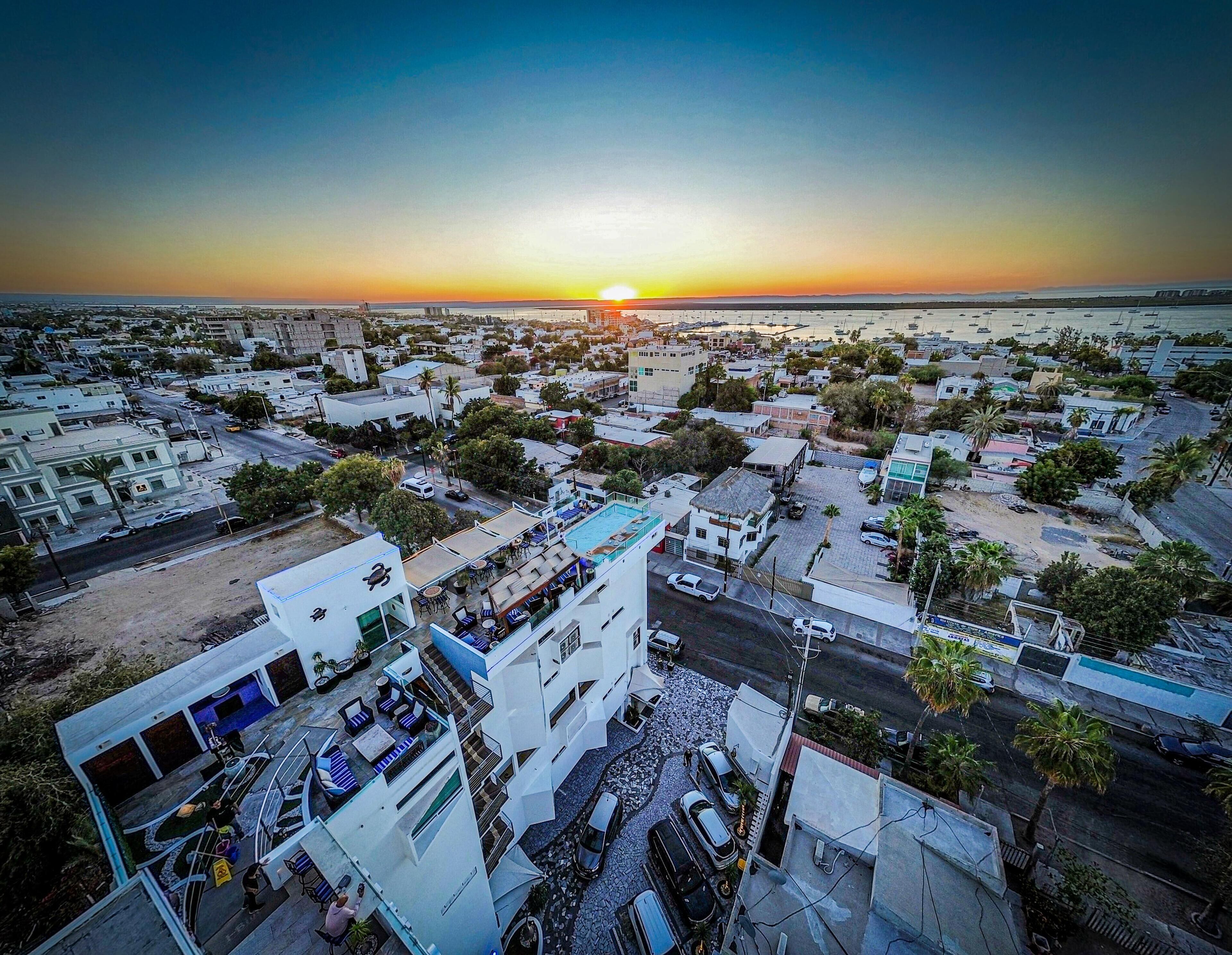 Vista aérea de un pueblo costero al atardecer, con un edificio destacado que cuenta con piscina en la azotea y varios pisos.