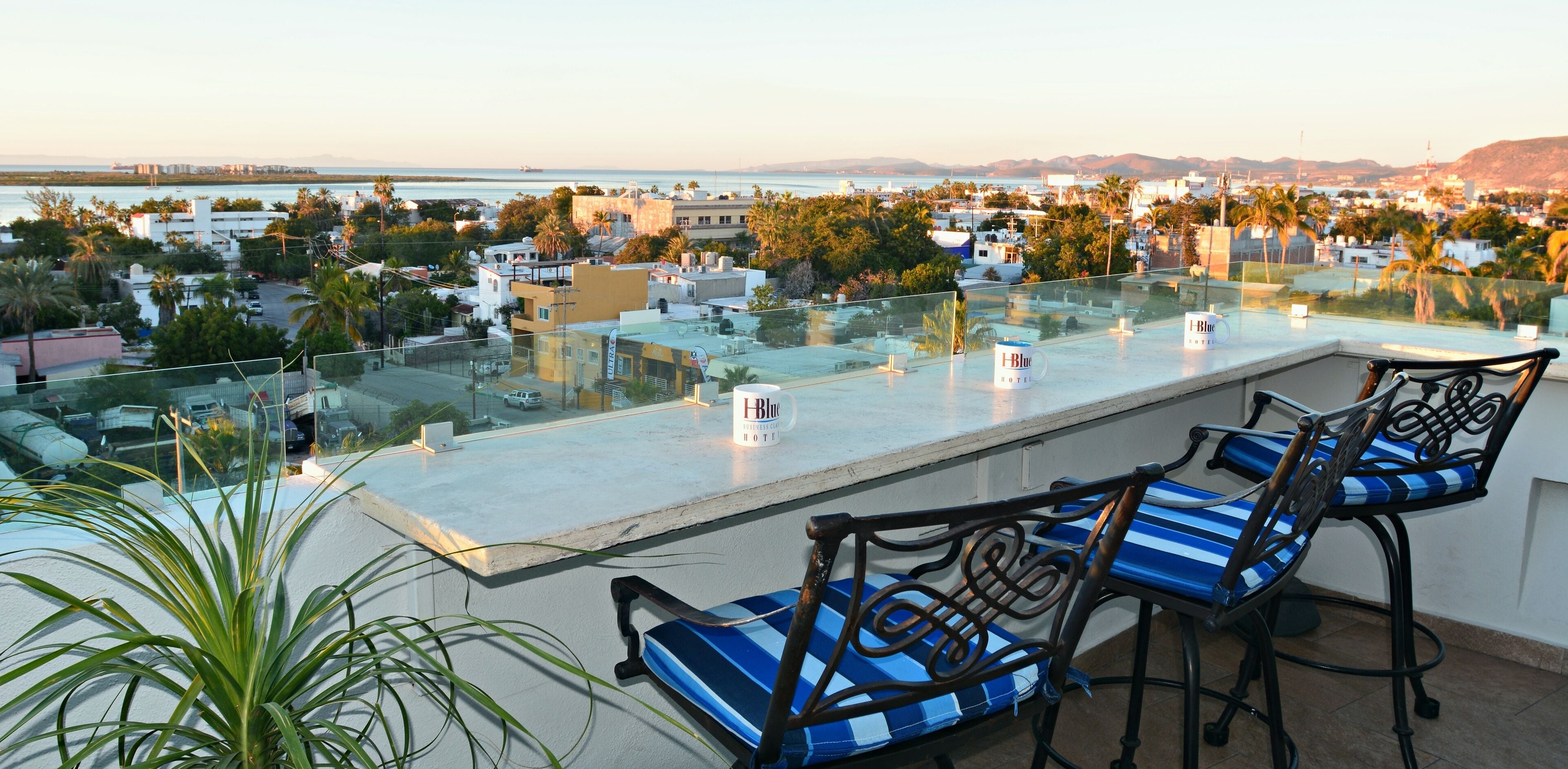 A rooftop terrace with a glass balustrade, two blue-striped chairs, and a sign for 'Blue Hotel'.