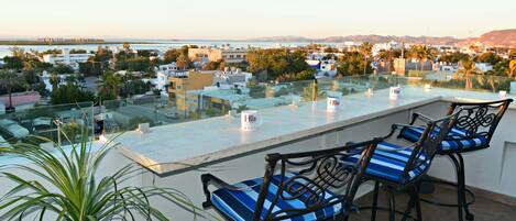 A rooftop terrace with a glass balustrade, two blue-striped chairs, and a sign for 'Blue Hotel'.
