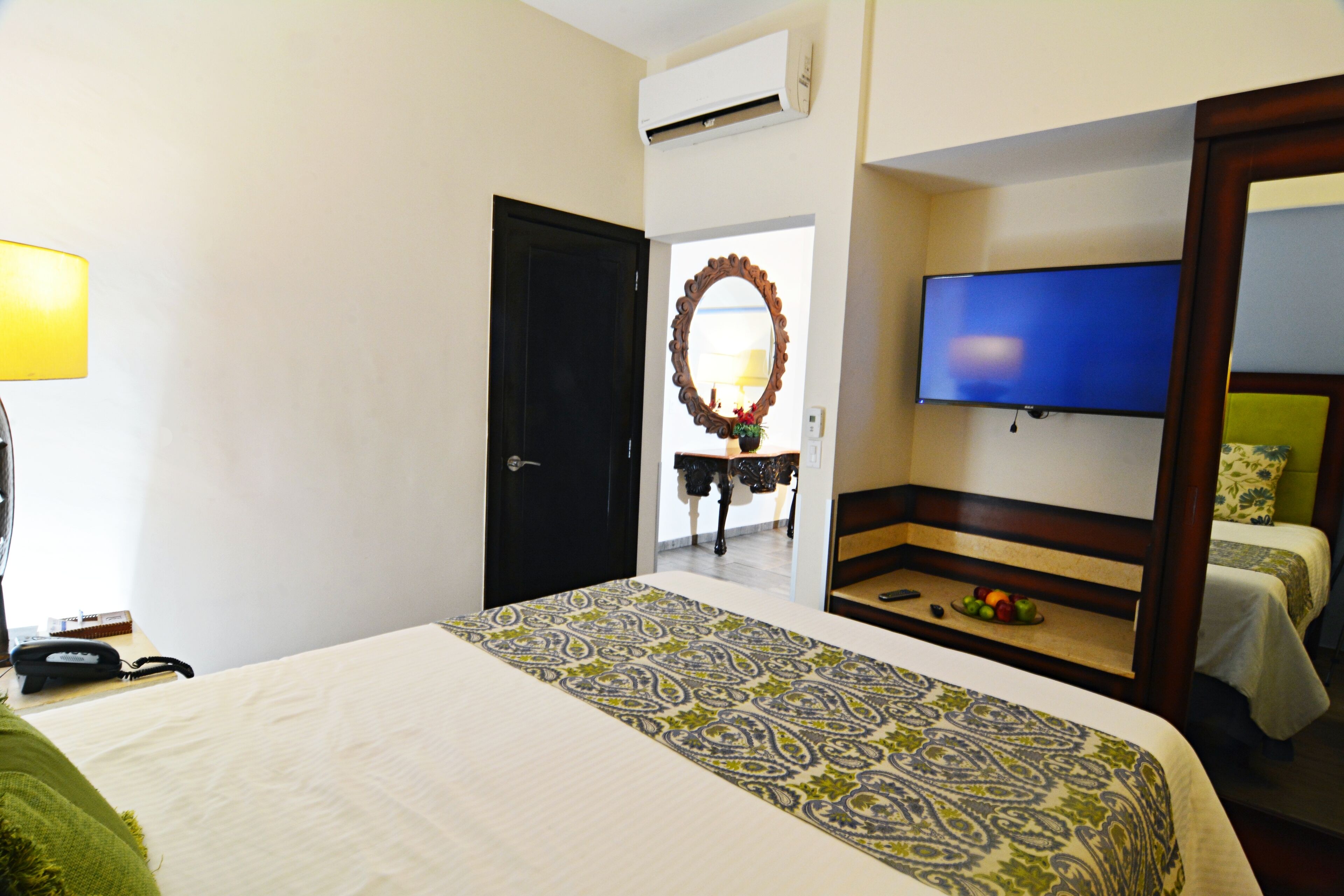 Camera d'albergo con un letto, una TV, una scrivania con una lampada e uno specchio.