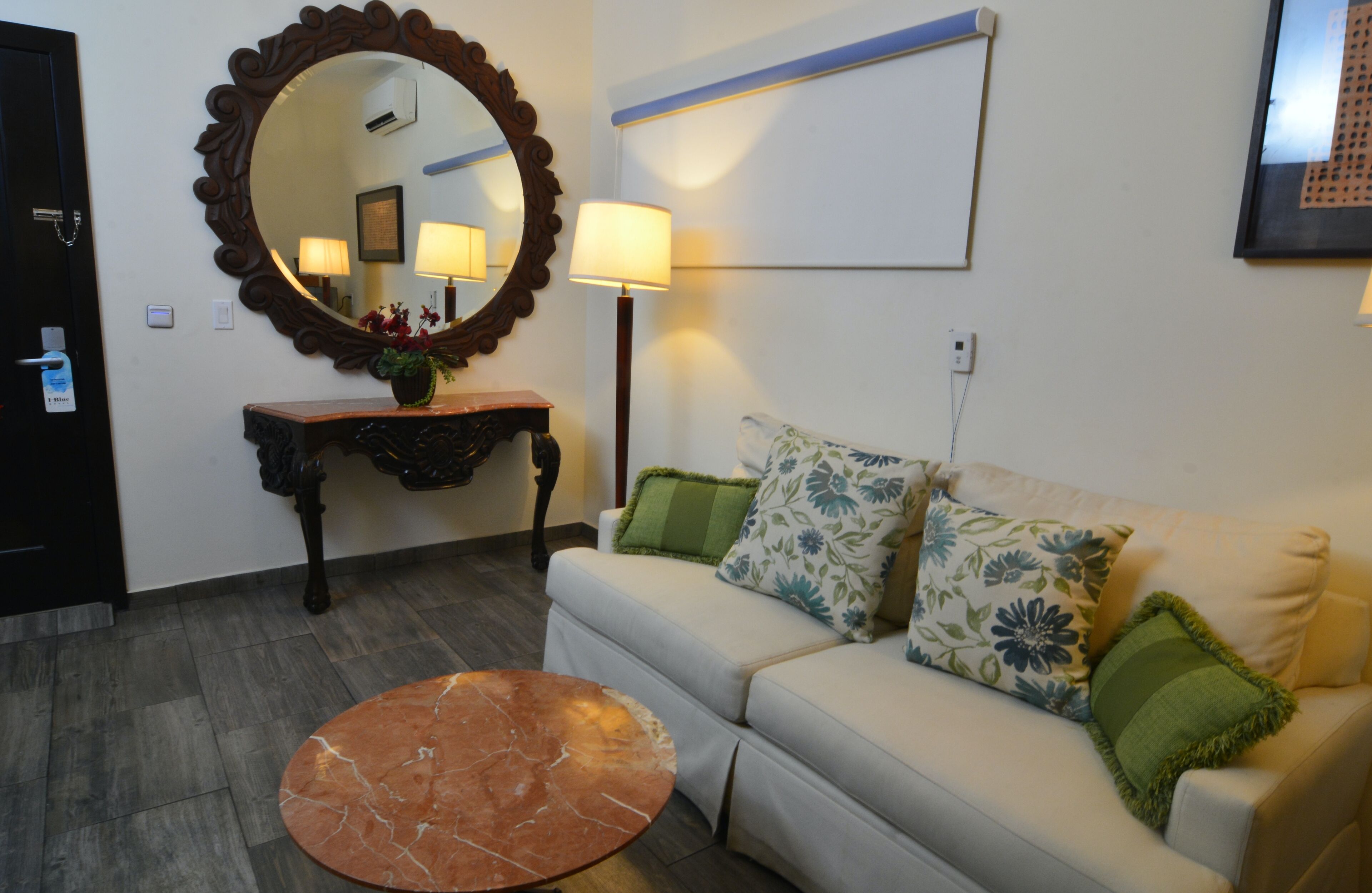 A living room with a sofa, a round coffee table, a mirror, a lamp, and a console table with a vase.