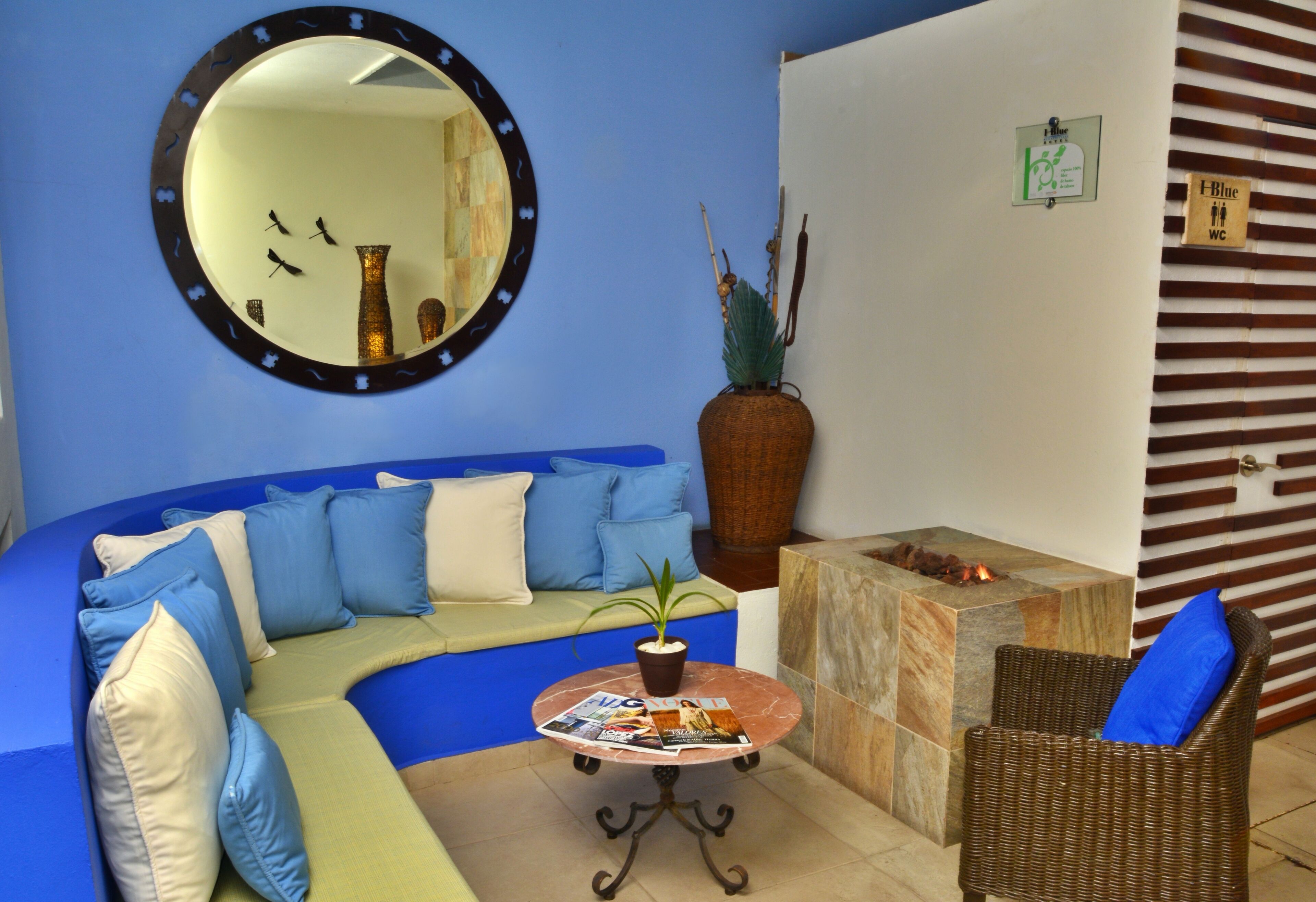 A room with a blue sofa, a round table with magazines, a mirror, a potted plant, and a sign indicating a blue WC.