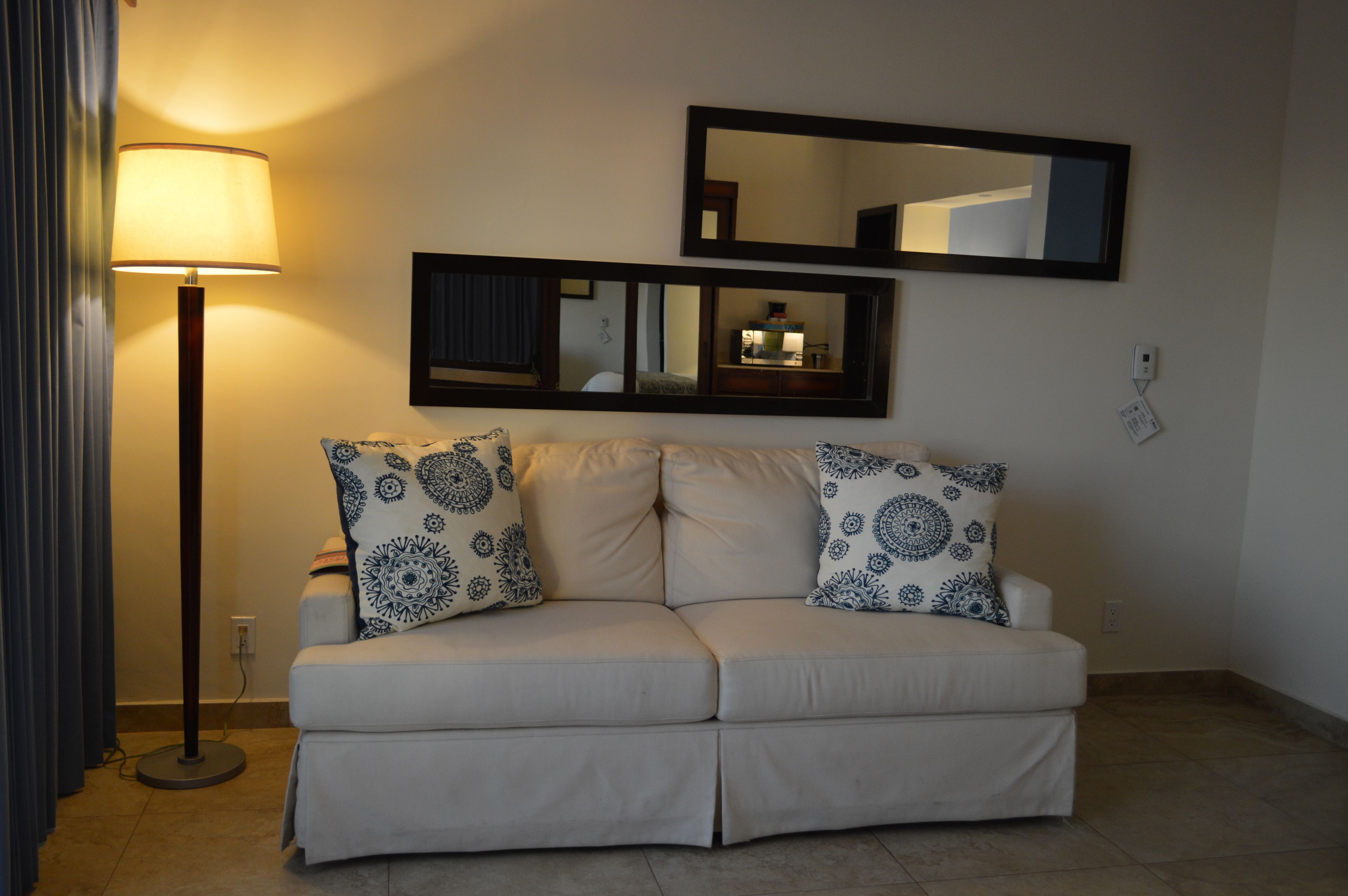 A neutral-colored sofa with patterned cushions, a floor lamp, and two wall mirrors.