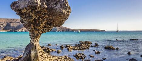 Una costa rocosa con aguas azules cristalinas y una formación rocosa destacada.