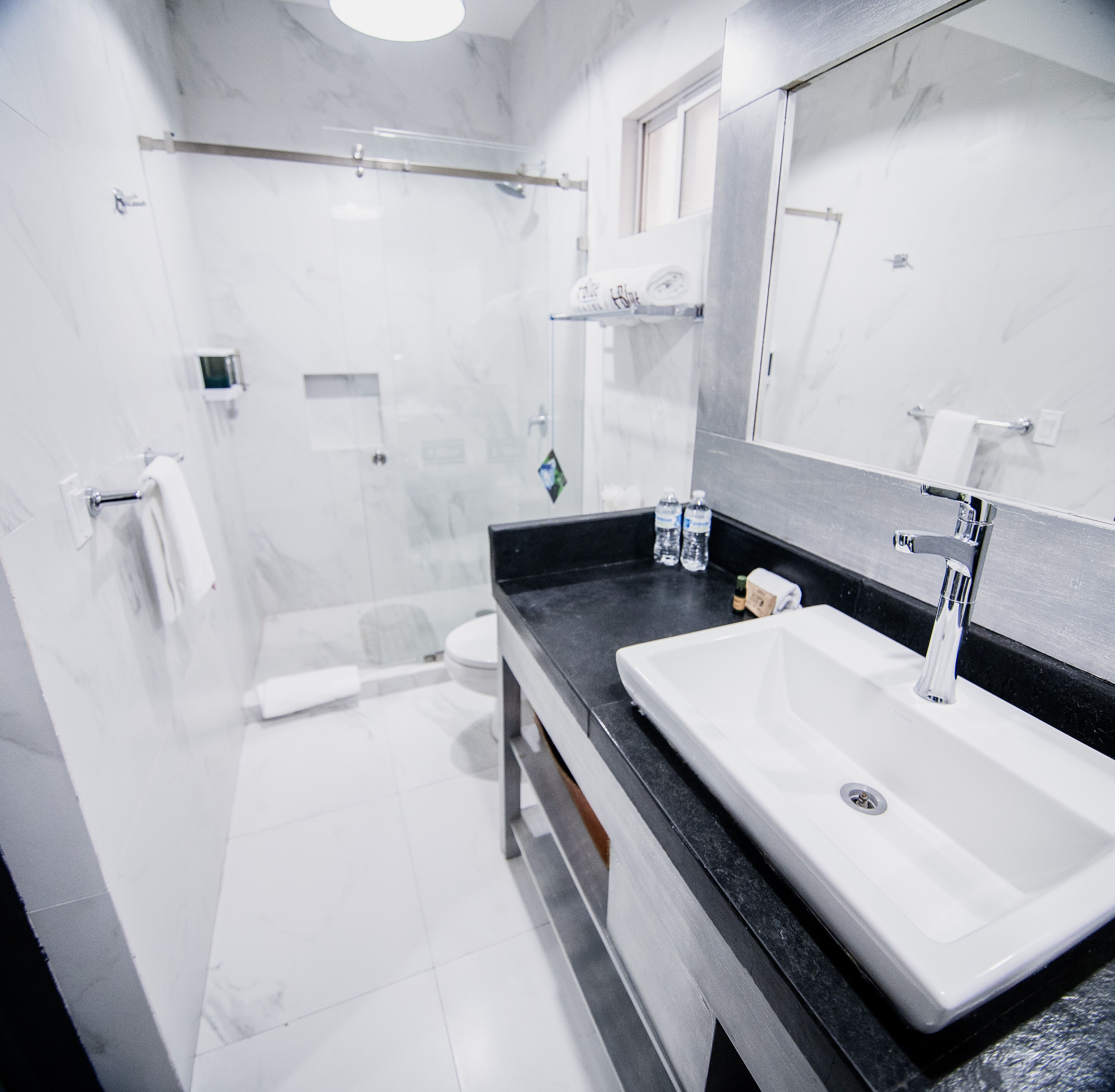 Une salle de bain moderne avec un grand miroir, un plan de toilette noir, un lavabo blanc et un espace douche.