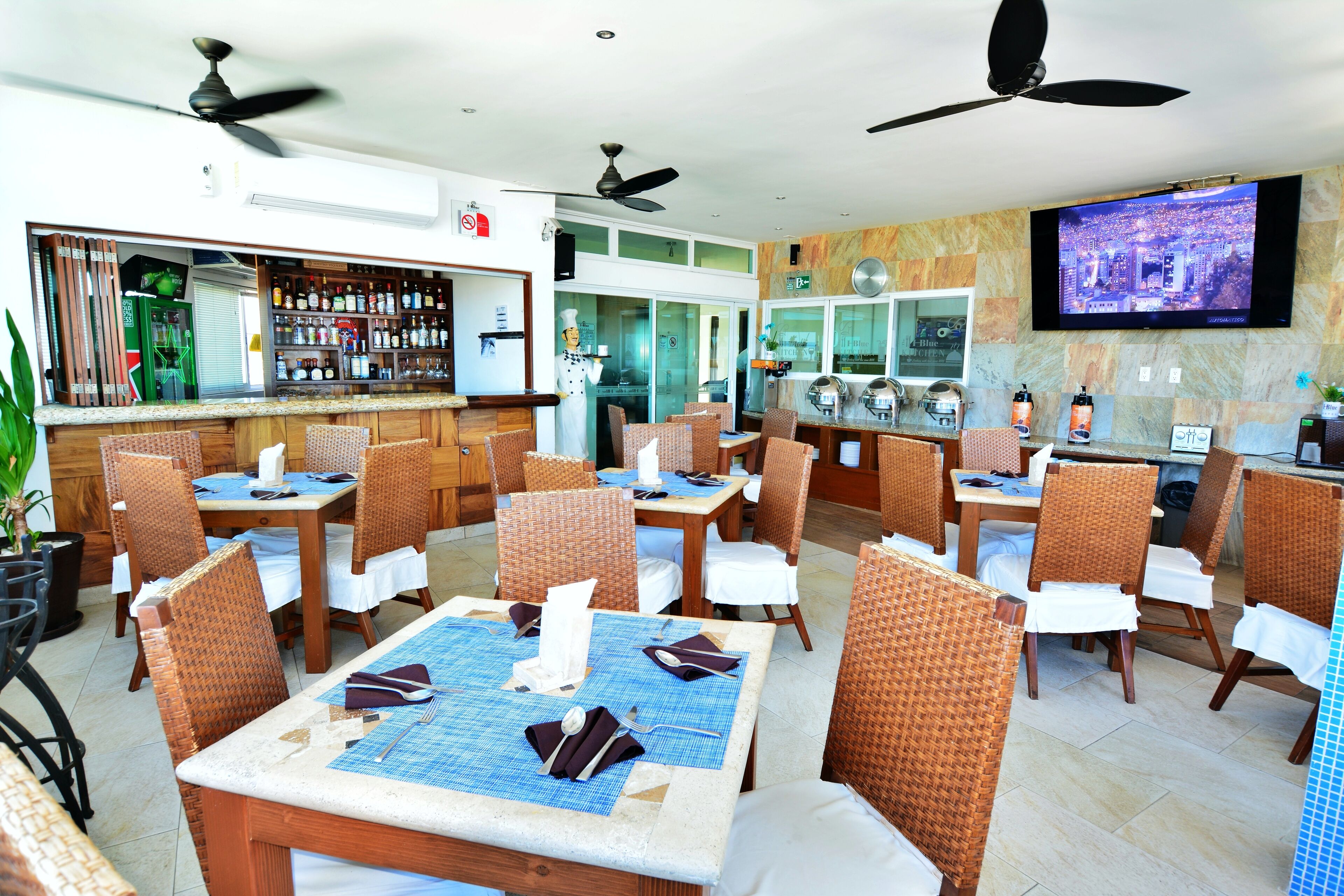 A restaurant with multiple tables and chairs, a bar area, and a television screen on the wall.