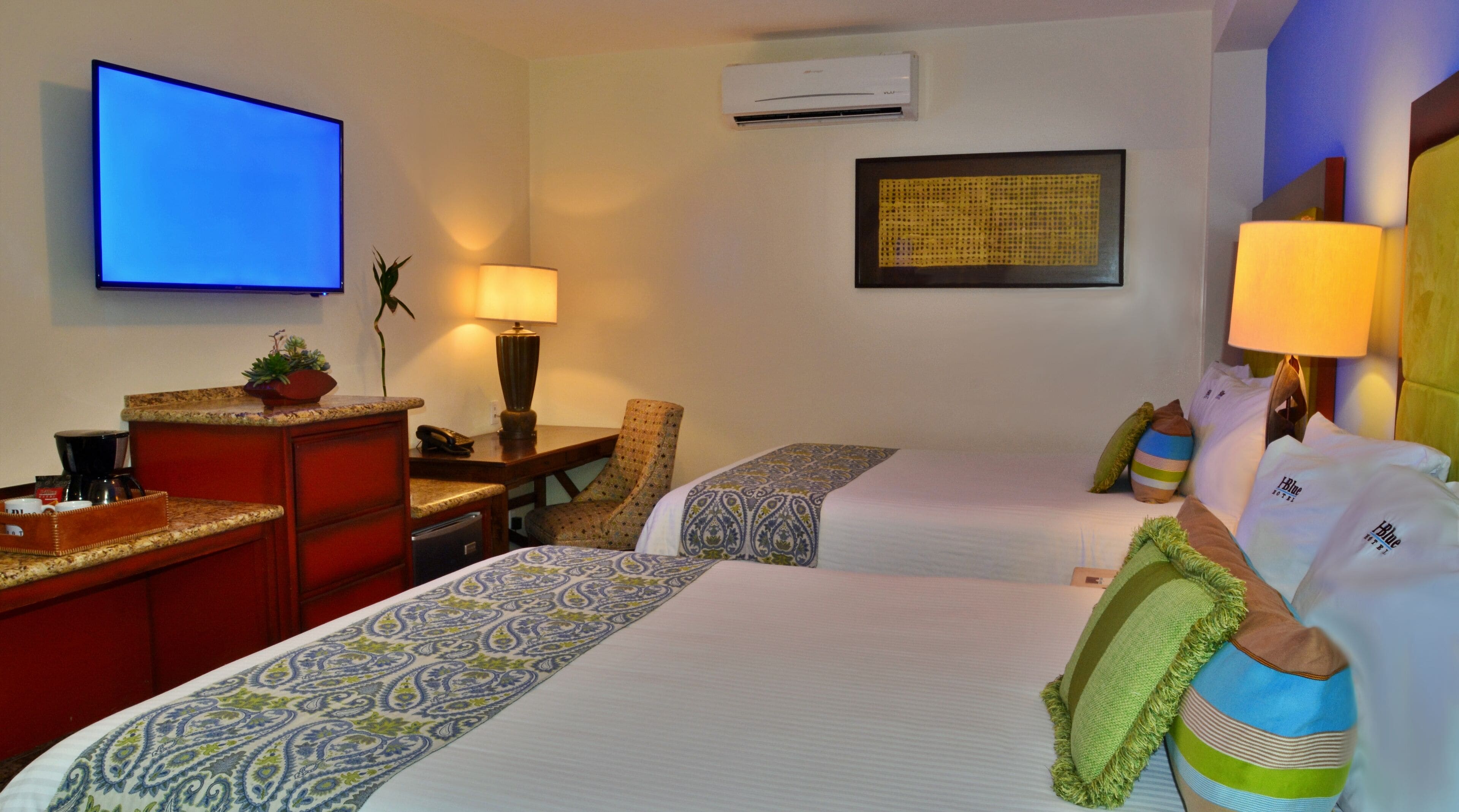 Une chambre d’hôtel avec deux lits, une télévision, un bureau avec une machine à café, une chaise et un climatiseur fixé au mur.