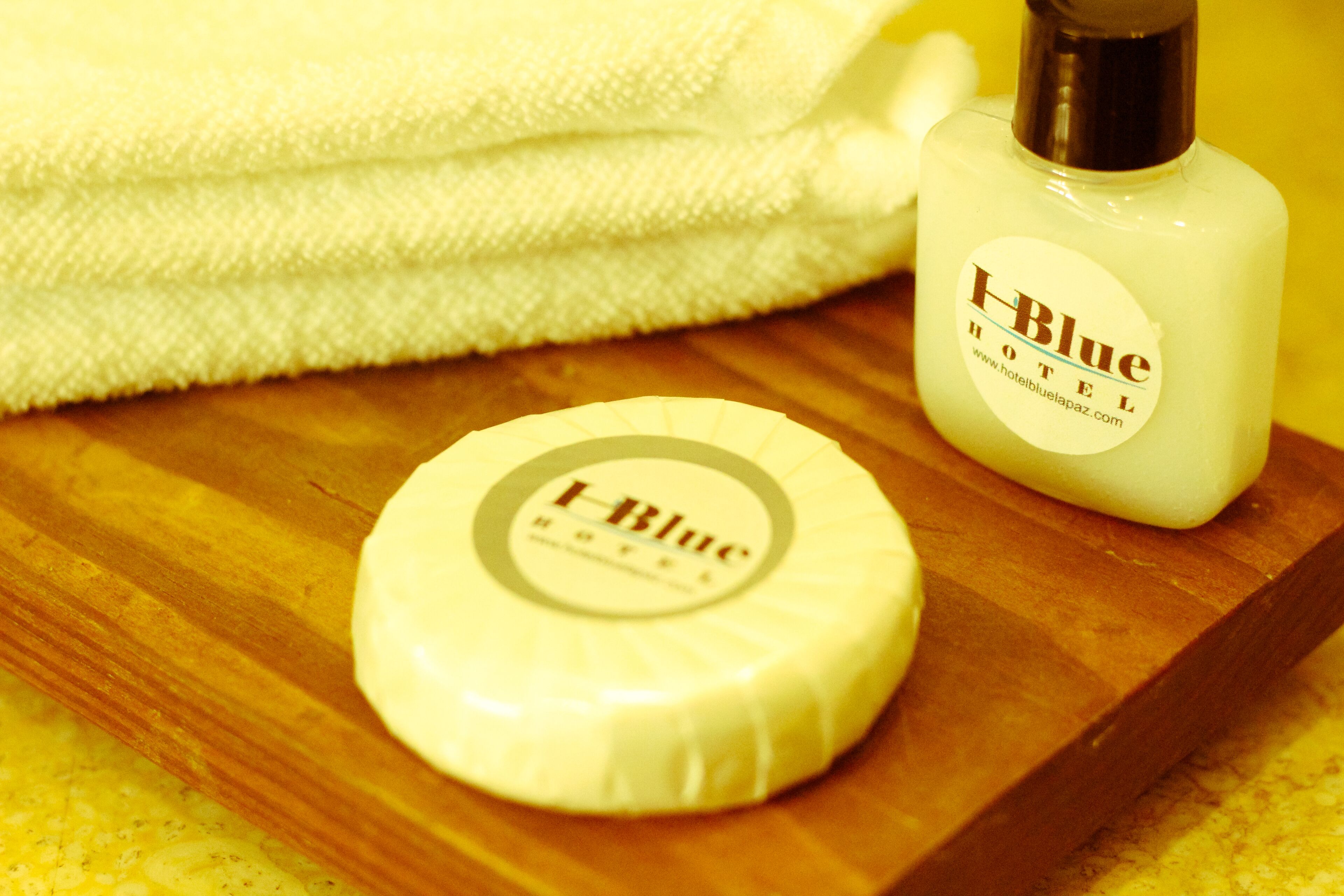 A soap bar and a bottle of lotion on a wooden tray with a folded towel in the background.