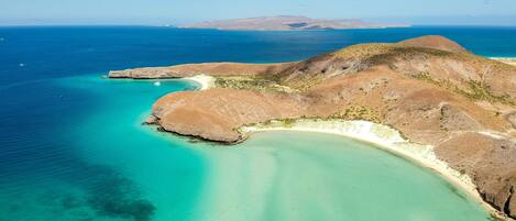 An aerial view of a coastal landscape with clear turquoise waters, sandy beaches, and rocky hills.