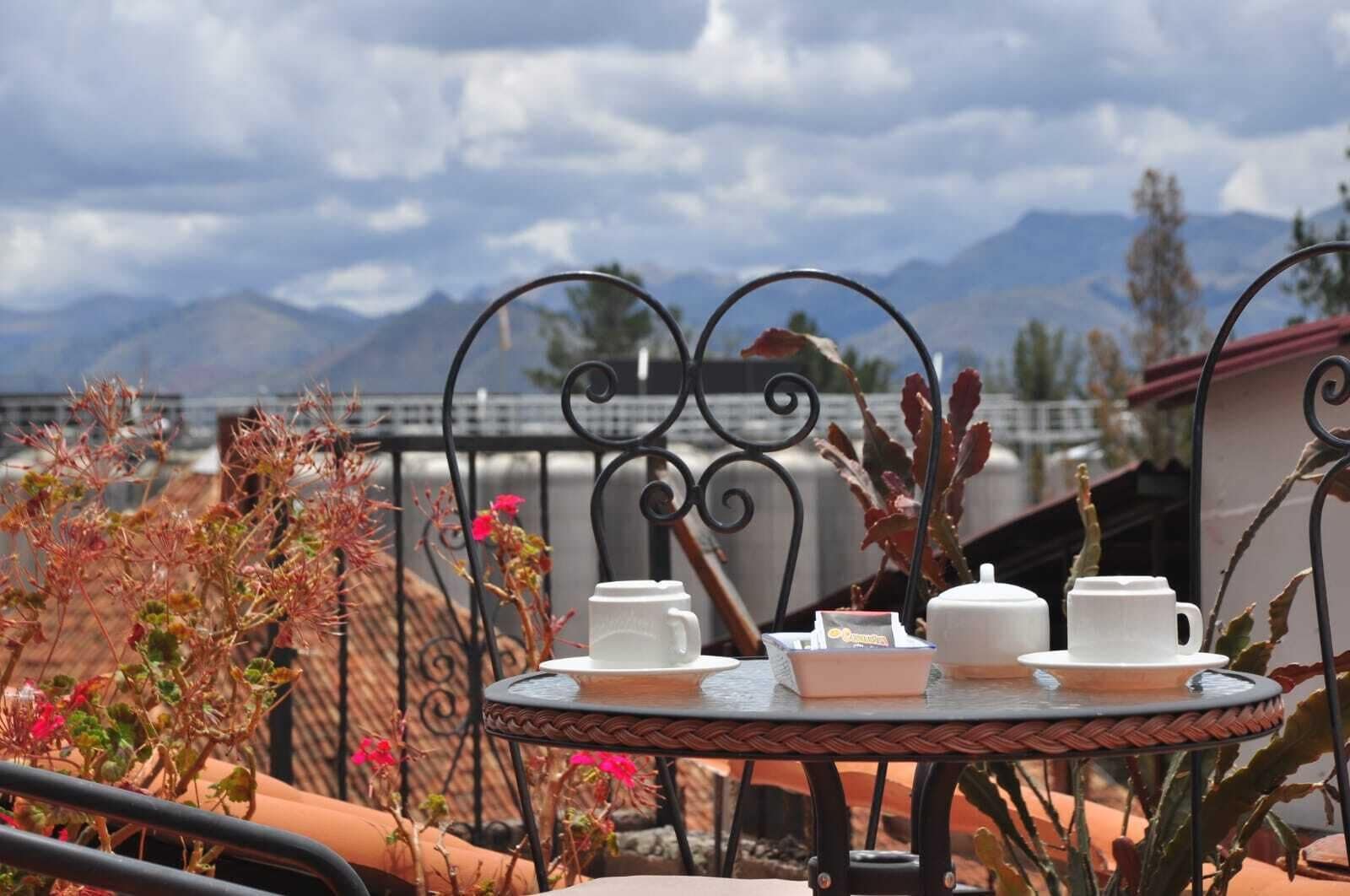 A round table with white teapots and cups, set against a backdrop of mountains and a cloudy sky.