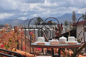 A round table with white teapots and cups, set against a backdrop of mountains and a cloudy sky. - Pumamarca Guest House (Cusco)
