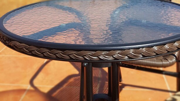 A round glass table with a woven edge, set on a tiled patio with a metal railing in the background. - Pumamarca Guest House (Cusco)
