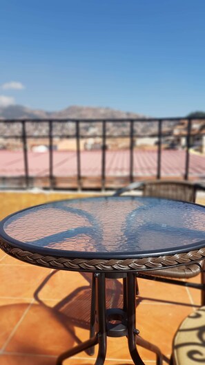 A round glass table with a woven edge, set on a tiled patio with a metal railing in the background. - Pumamarca Guest House (Cusco)