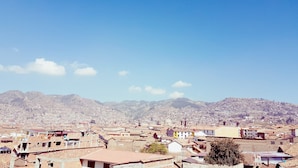 A cityscape with a mountainous backdrop, featuring densely packed buildings and a clear sky. - Pumamarca Guest House (Cusco)