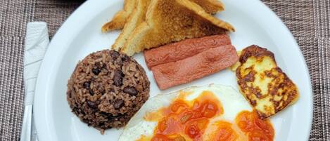 A breakfast plate with toast, sausage, beans, and a fried egg with tomato sauce.
