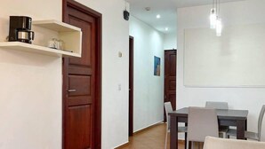 A spacious living area with a sofa, a dining table with chairs, a coffee machine on a shelf, and a large window. - RDG Hotel (Managua)