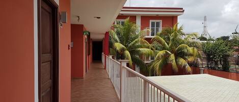 A corridor with a tiled floor, a balcony with a white railing, and a building with a red facade.