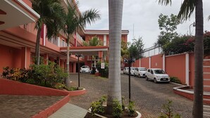 A multi-story building with a red facade, a paved driveway, and several parked cars. - RDG Hotel (Managua)