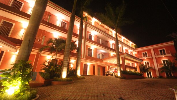 A multi-story hotel with a red facade, palm trees, and a paved driveway. - RDG Hotel (Managua)