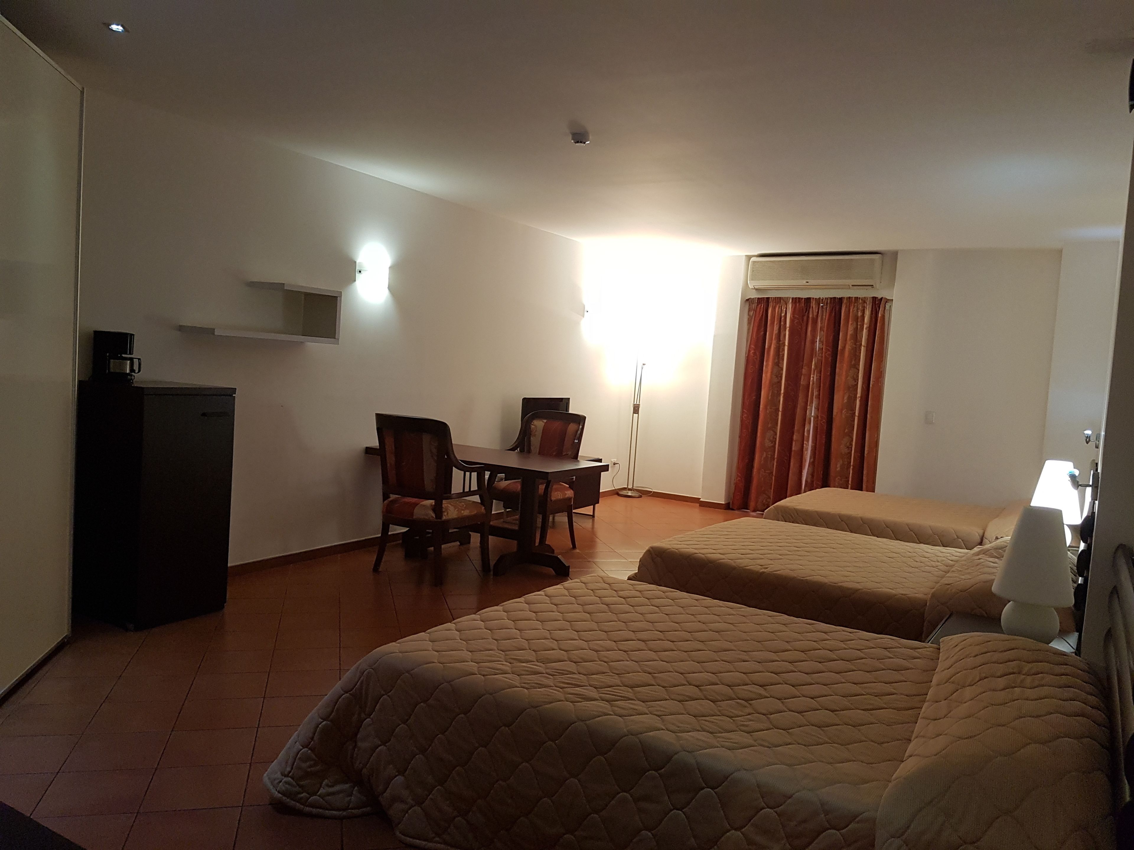 A hotel room with two beds, a desk with a chair, a coffee machine, and a window with curtains.