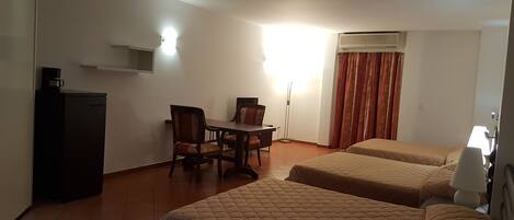 A hotel room with two beds, a desk with a chair, a coffee machine, and a window with curtains.