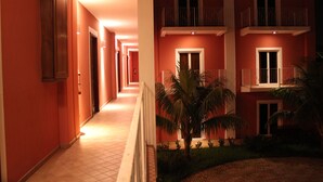 A corridor with a tiled floor, a palm tree, and a building with balconies and windows. - RDG Hotel (Managua)