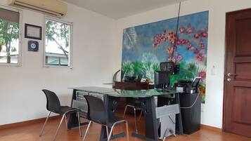Une chambre d’hôtel équipée d’un bureau, de chaises, d’un ordinateur et d’un grand tableau représentant des motifs floraux accroché au mur.