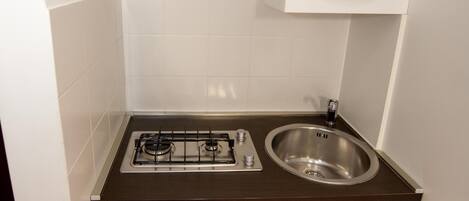Una cocina compacta con estufa a gas, pileta de acero inoxidable, gabinetes blancos y extractor.